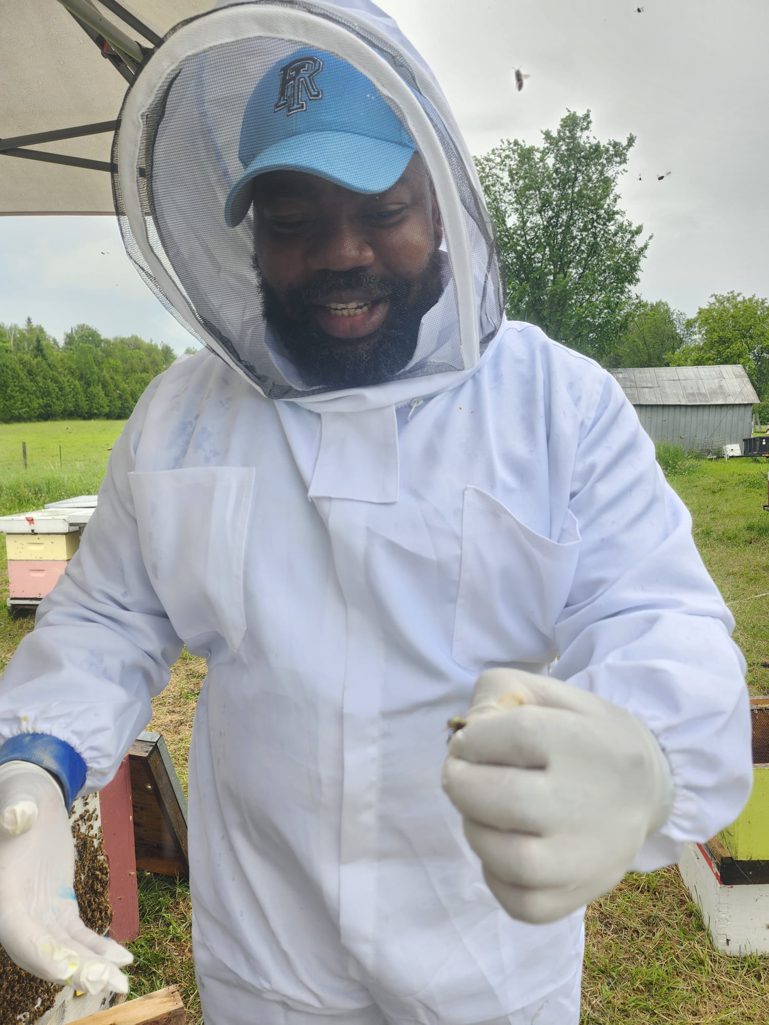 Taiwo Amoo holding queen marking cage in apiary